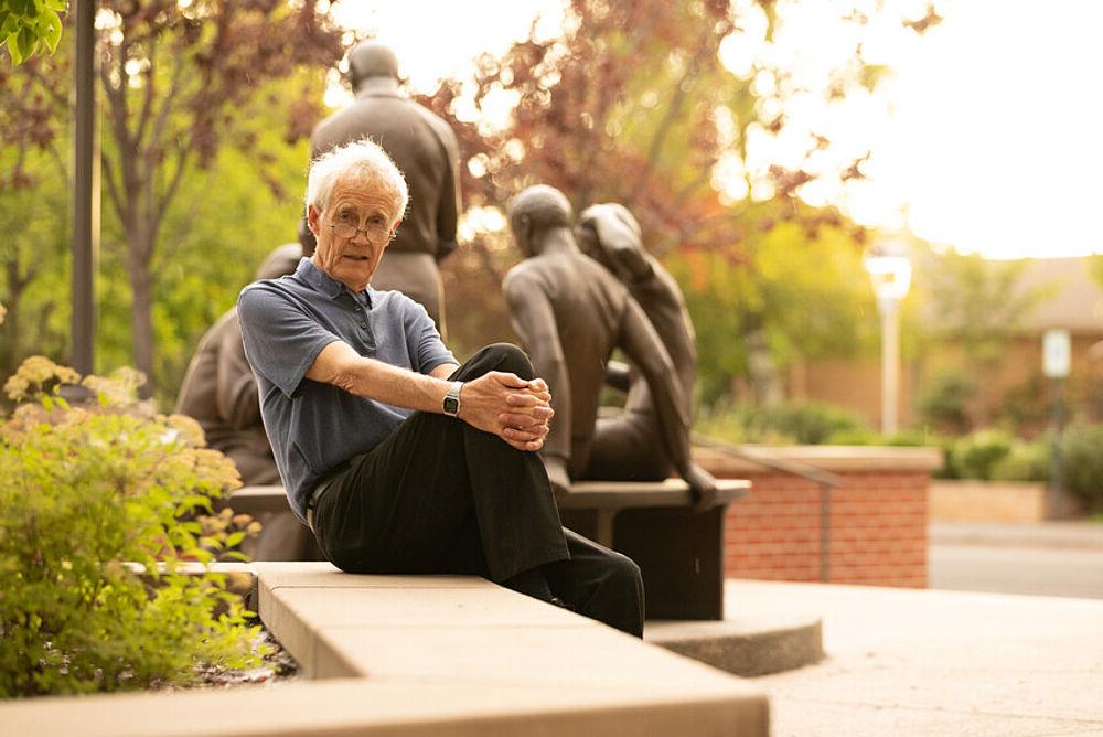 elderly man sitting in front of a statue and trees